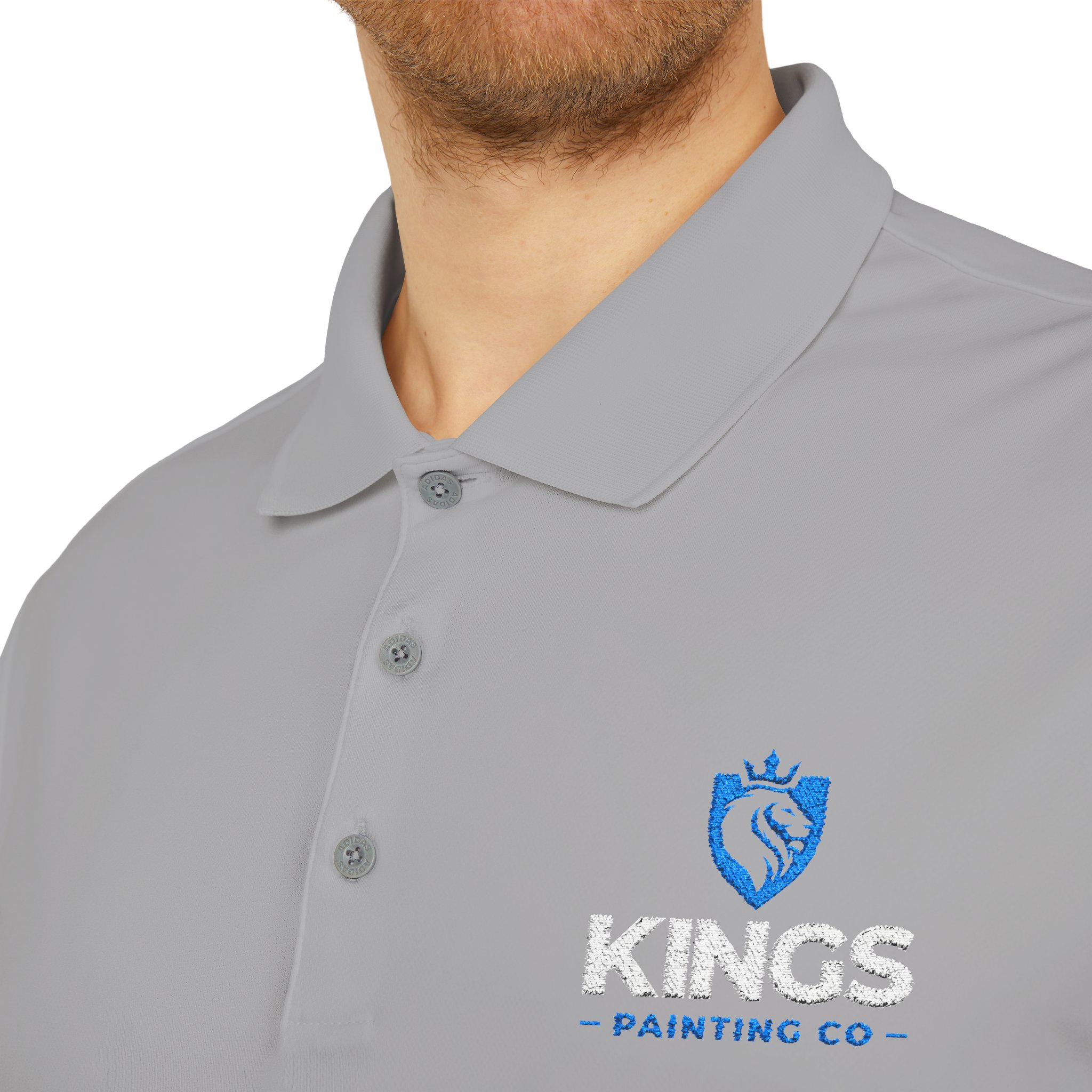 A person is wearing the Kings Painting Co. Performance Polo by Under Armour® in light gray, featuring a blue KINGS PAINTING CO logo and a lion emblem embroidered on the left chest. Only the lower face and upper torso are visible.