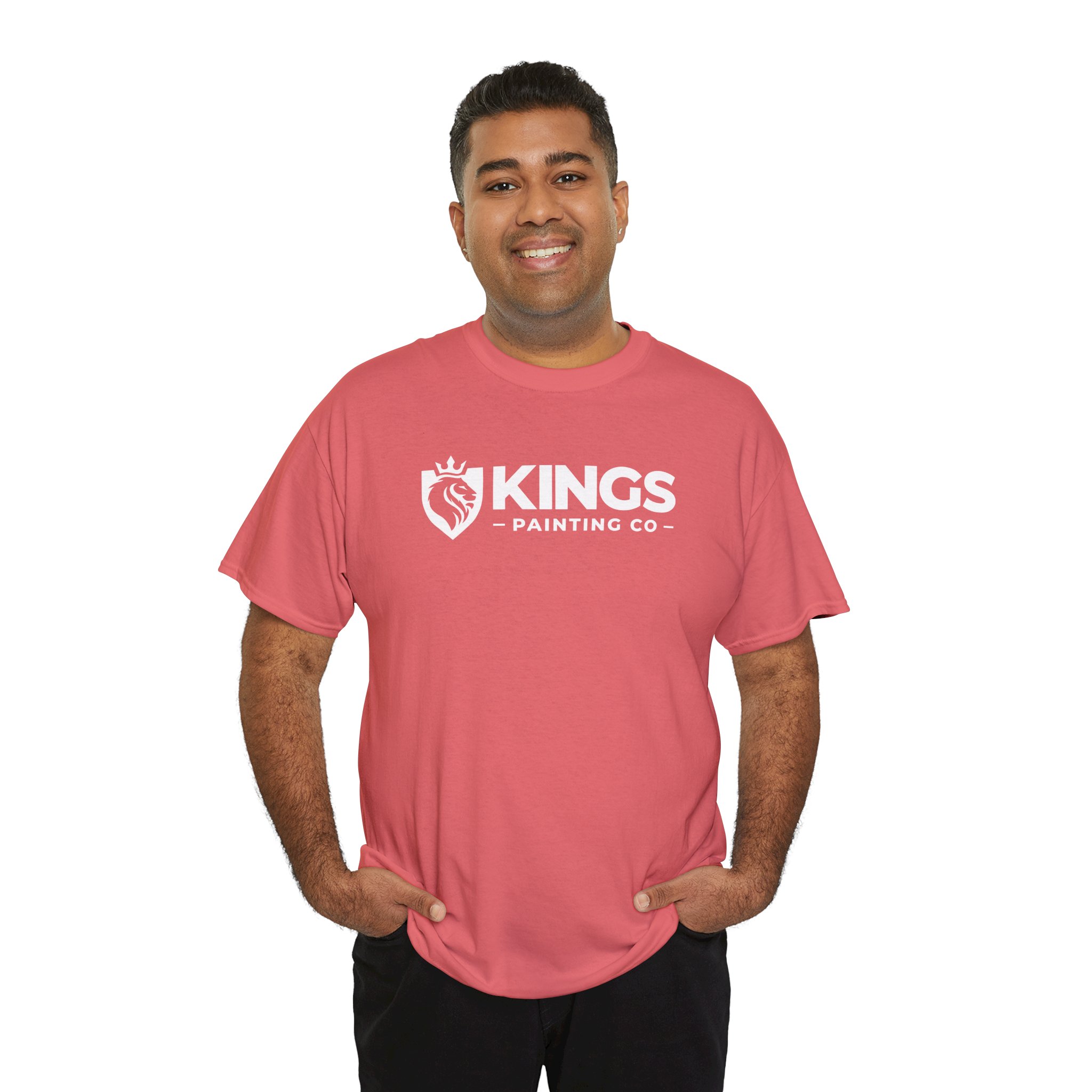 A smiling person stands with hands in pockets, wearing the Kings Painting Co. Logo T‑Shirt (Classic) | Gildan Ultra Cotton (G5000) in pink, which features a lion logo on the front. The background is plain white.